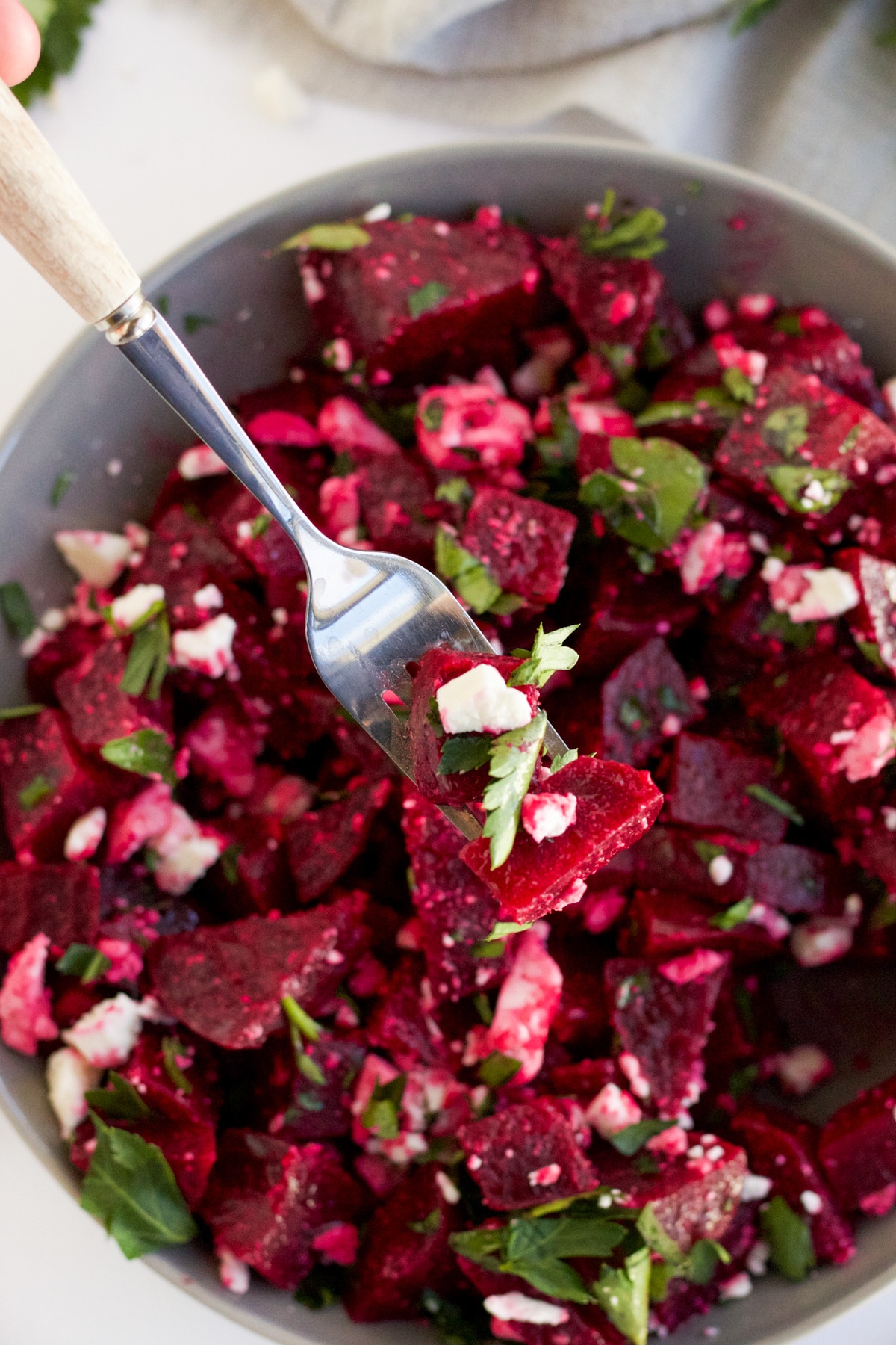 A fork with a bite of beetroot salad on it over bowl of beet salad.