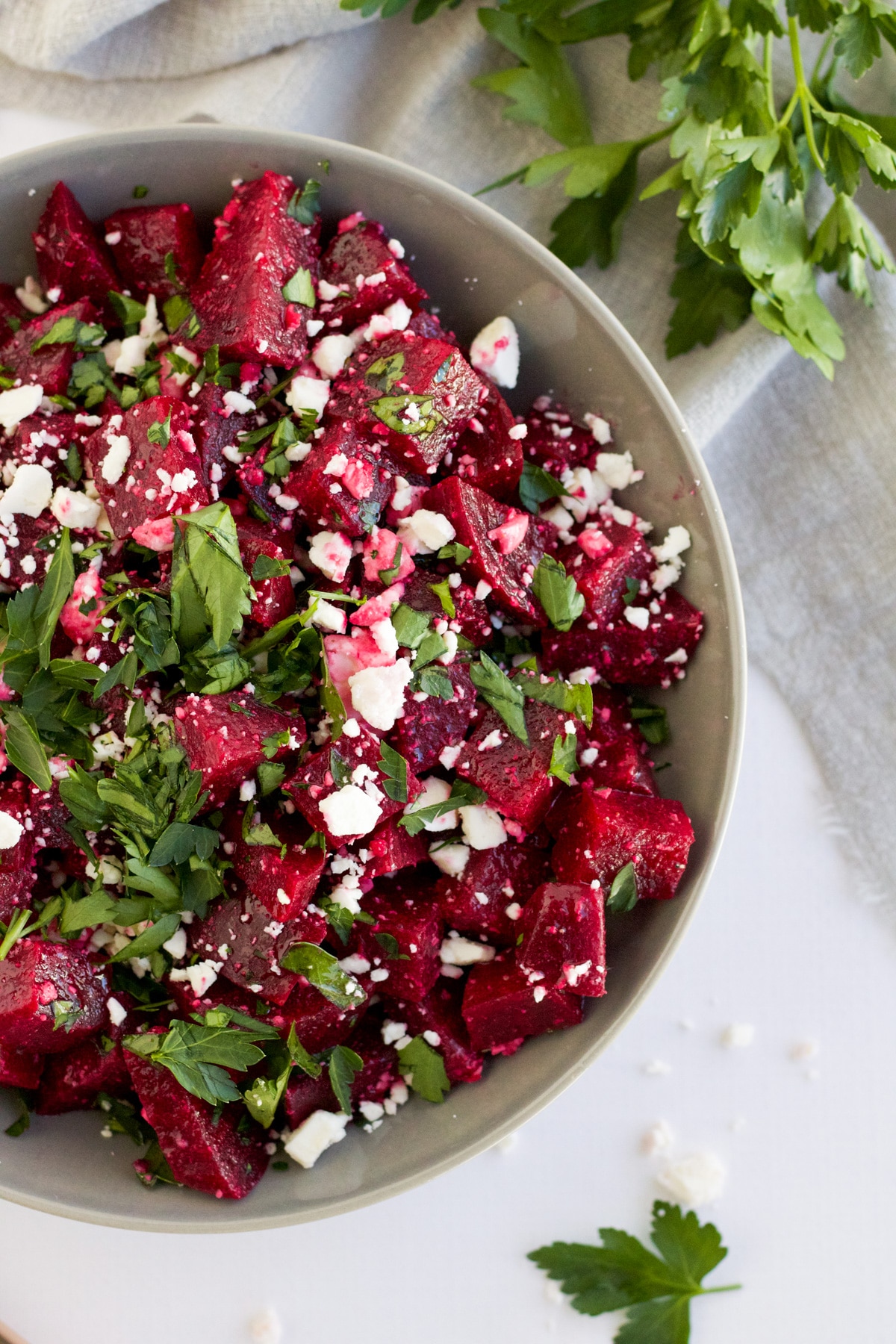 An overhead image of a beetroot salad in a grey bowl with beetroot, feta and parsley