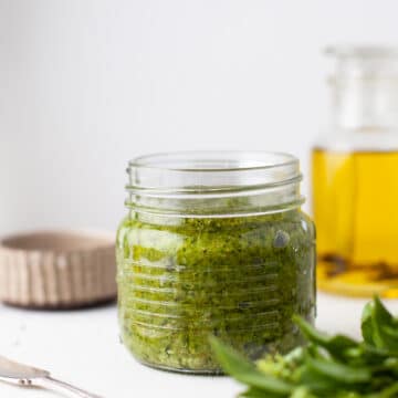 A jar of cashew pesto sauce with oil and basil around it.