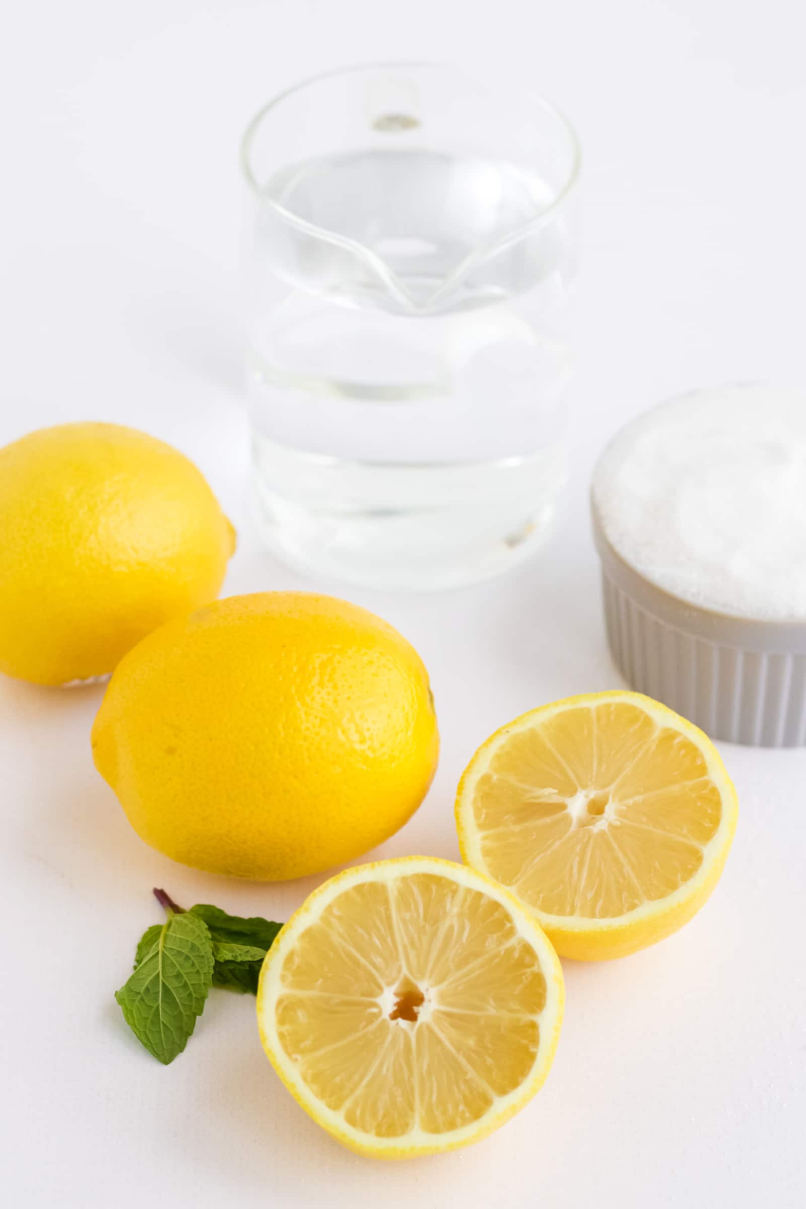 2 whole lemons 1 lemon sliced in half a pitcher of water and a bowl of sugar.