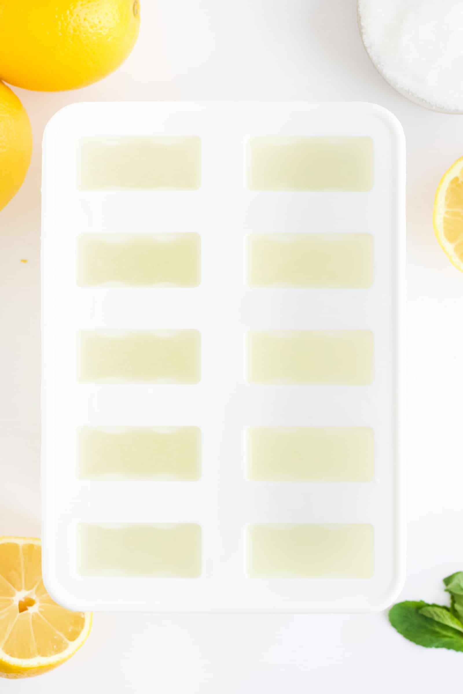 popsicle mold filled with lemonade and lemons and sugar in the background