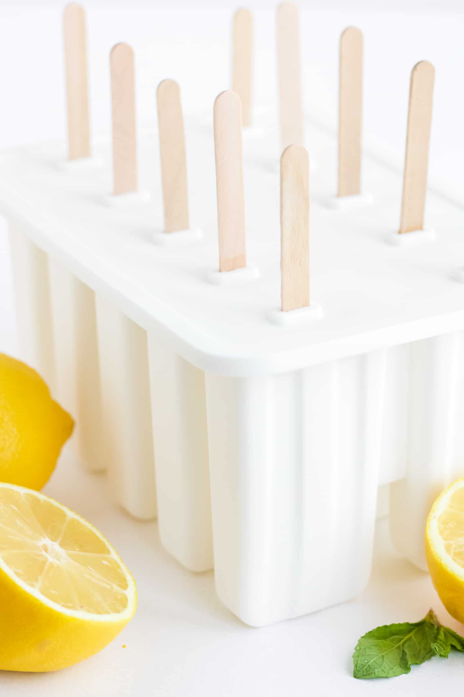 10 lemonade popsicles in a mold with cut lemons in the foreground.