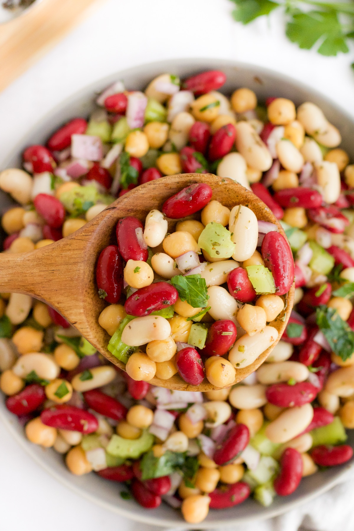 three bean salad being scooped by a wooden spoon