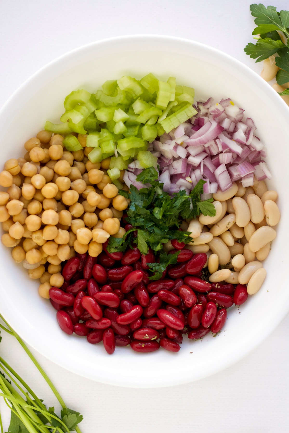 kidney, garbanzo, and cannelini beans in a white bowl with chopped celery and red onion and parsley