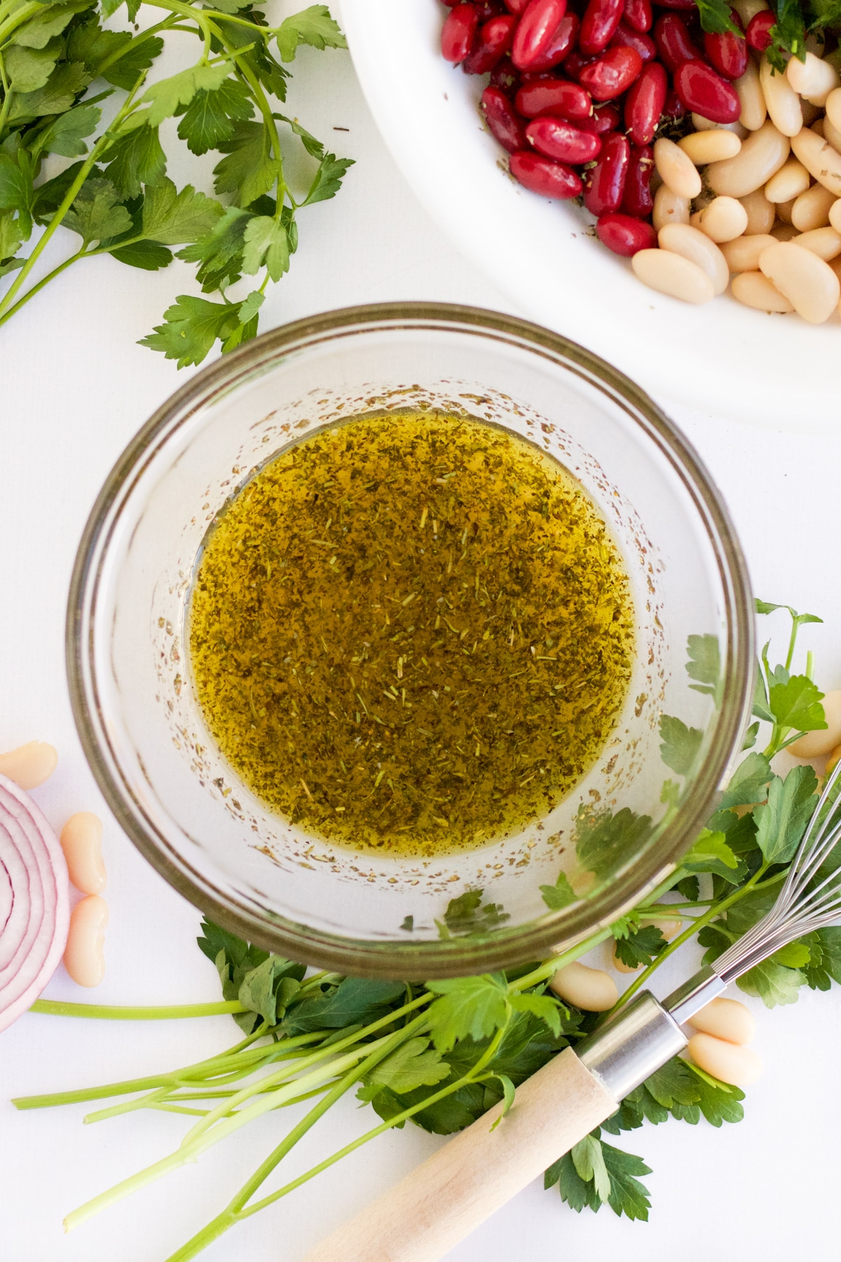 three bean salad dressing in a glass bowl with a whisk