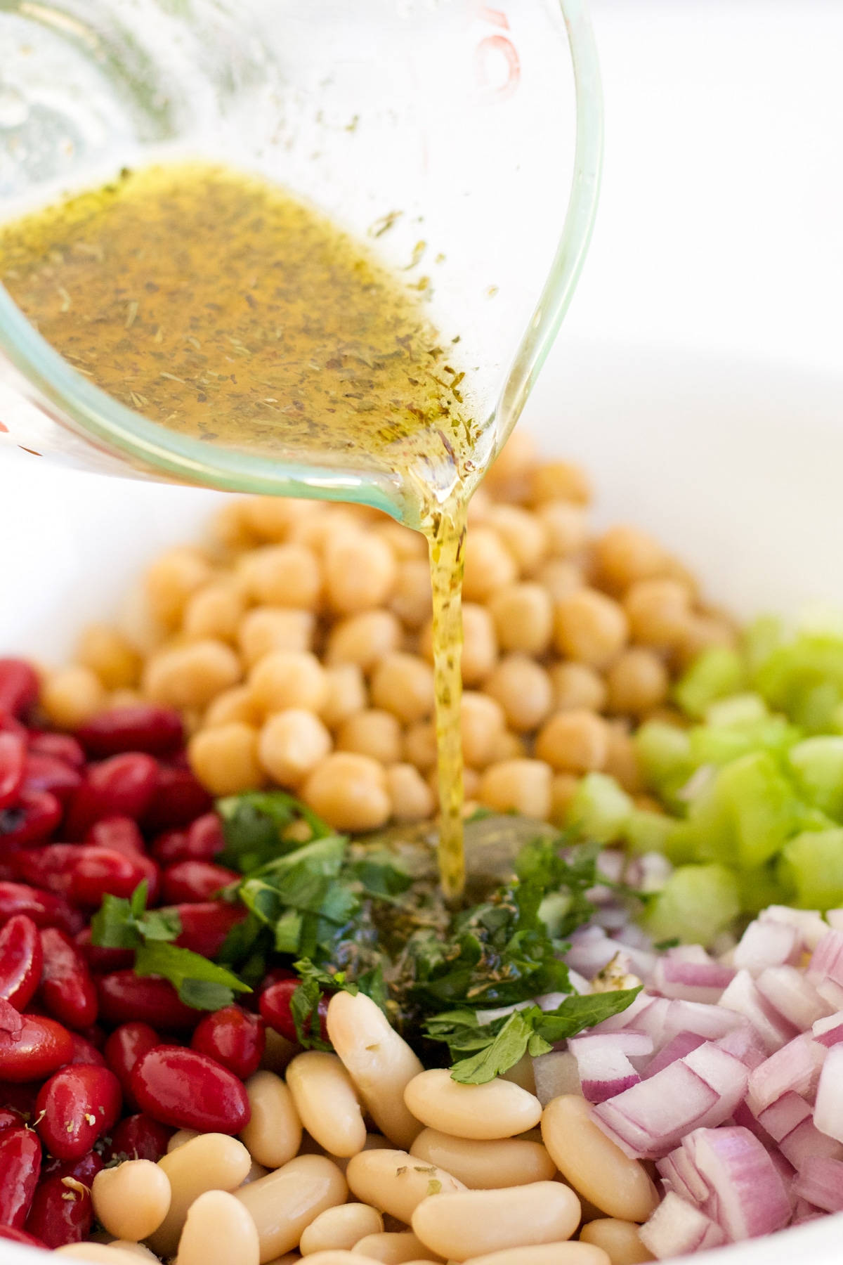 dressing being poured over a trio of beans and vegetables