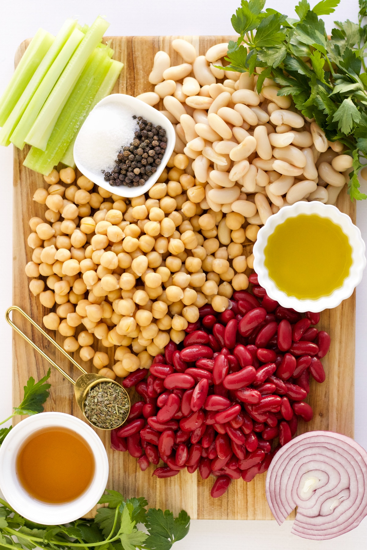 kidney, garbanzo, and cannellini beans. red onion, celery, parsely on a cutting board