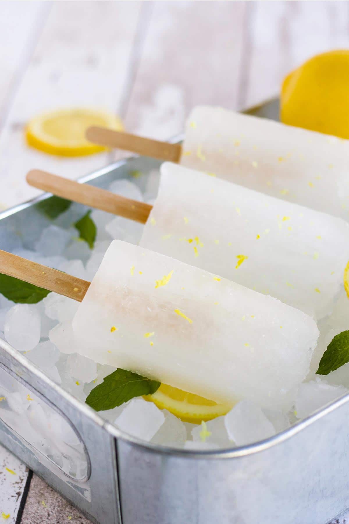3 lemonade popsicles on a metal tray of ice.
