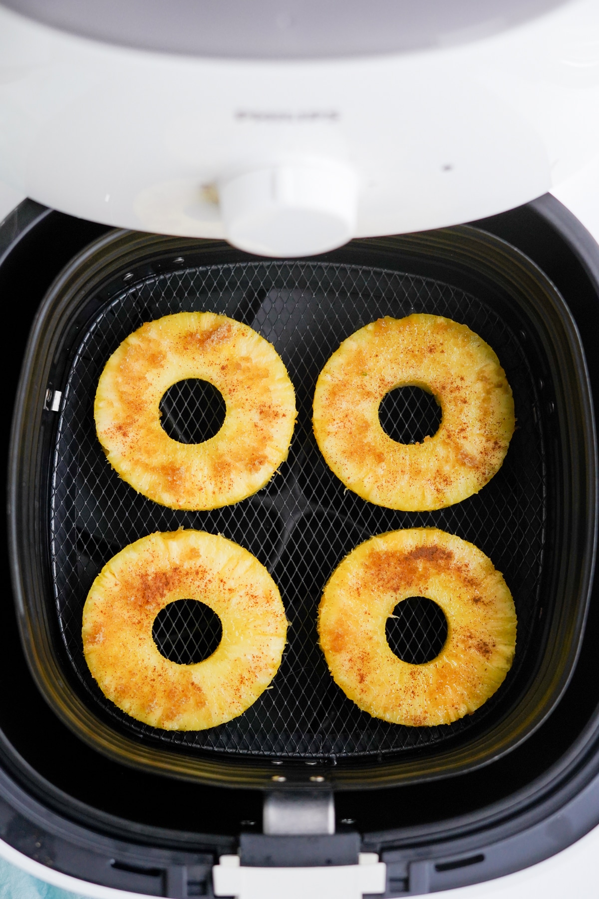 4 pineapple rings in an air fryer basket dusted with cinnamon and sugar