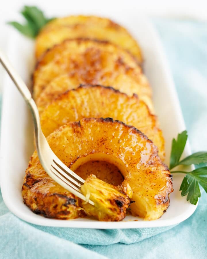 caramelized pineapple rings on white platter with fork