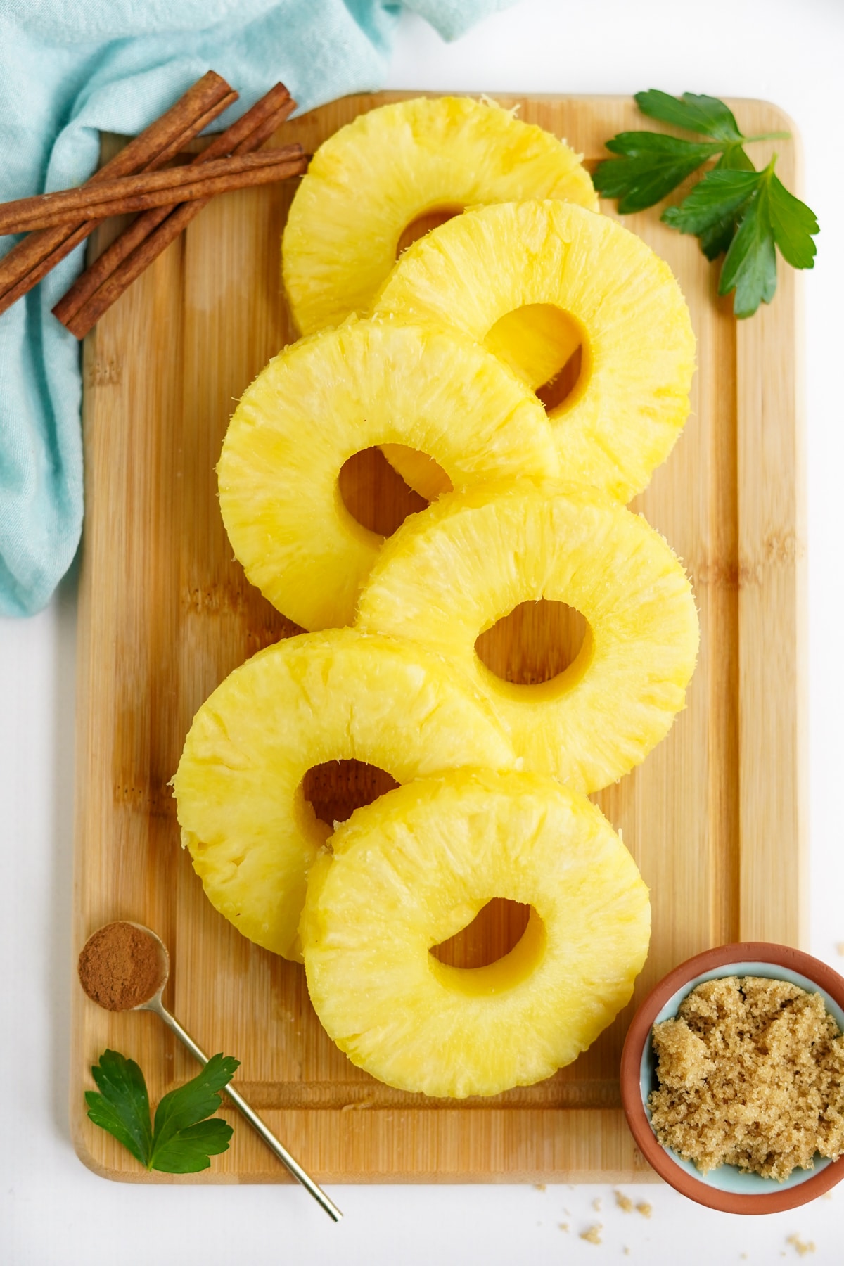 sliced fresh pineapple rings on a wooden cutting board with cinnamon and brown sugar mixture.