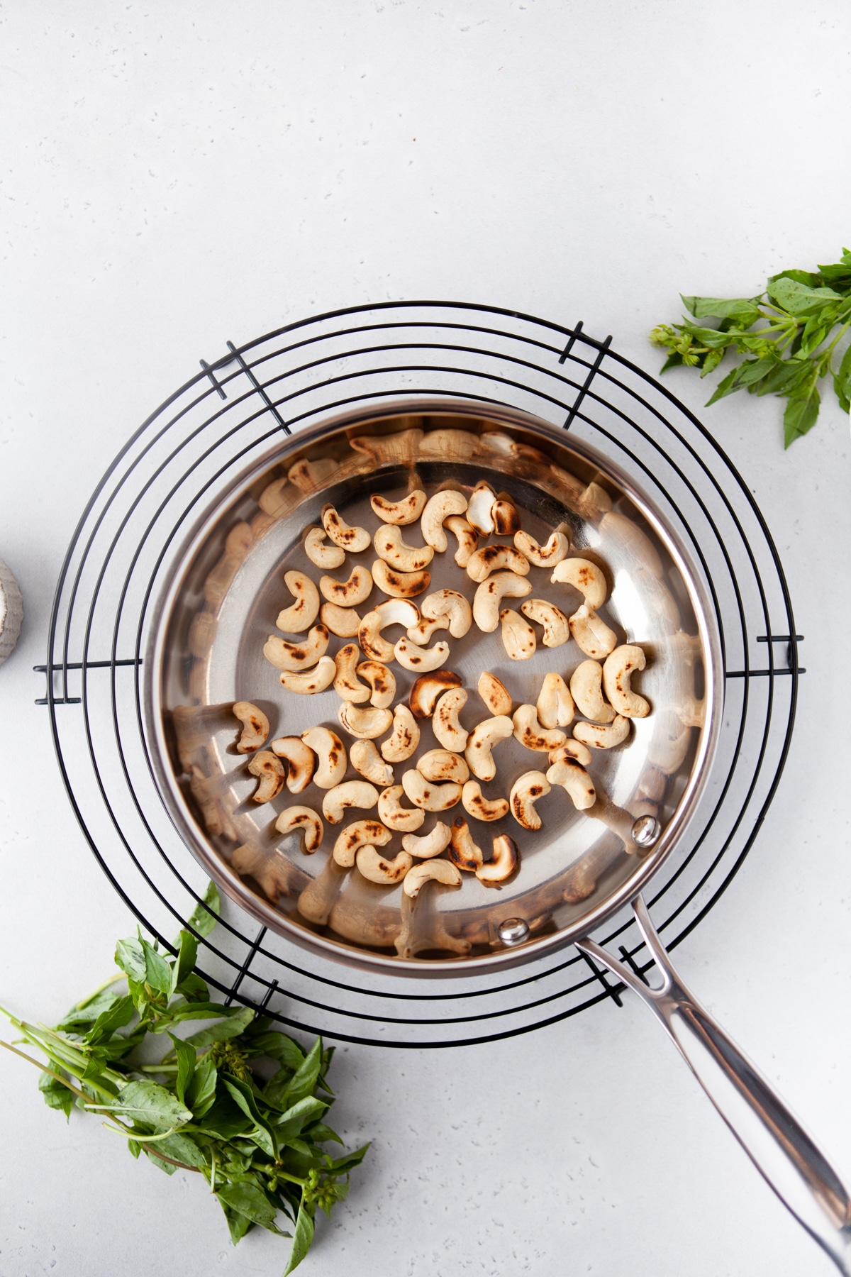 skillet with toasted whole cashews and sprigs of basil scattered around