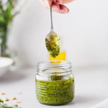 hand with spoon in a glass jar of pesto