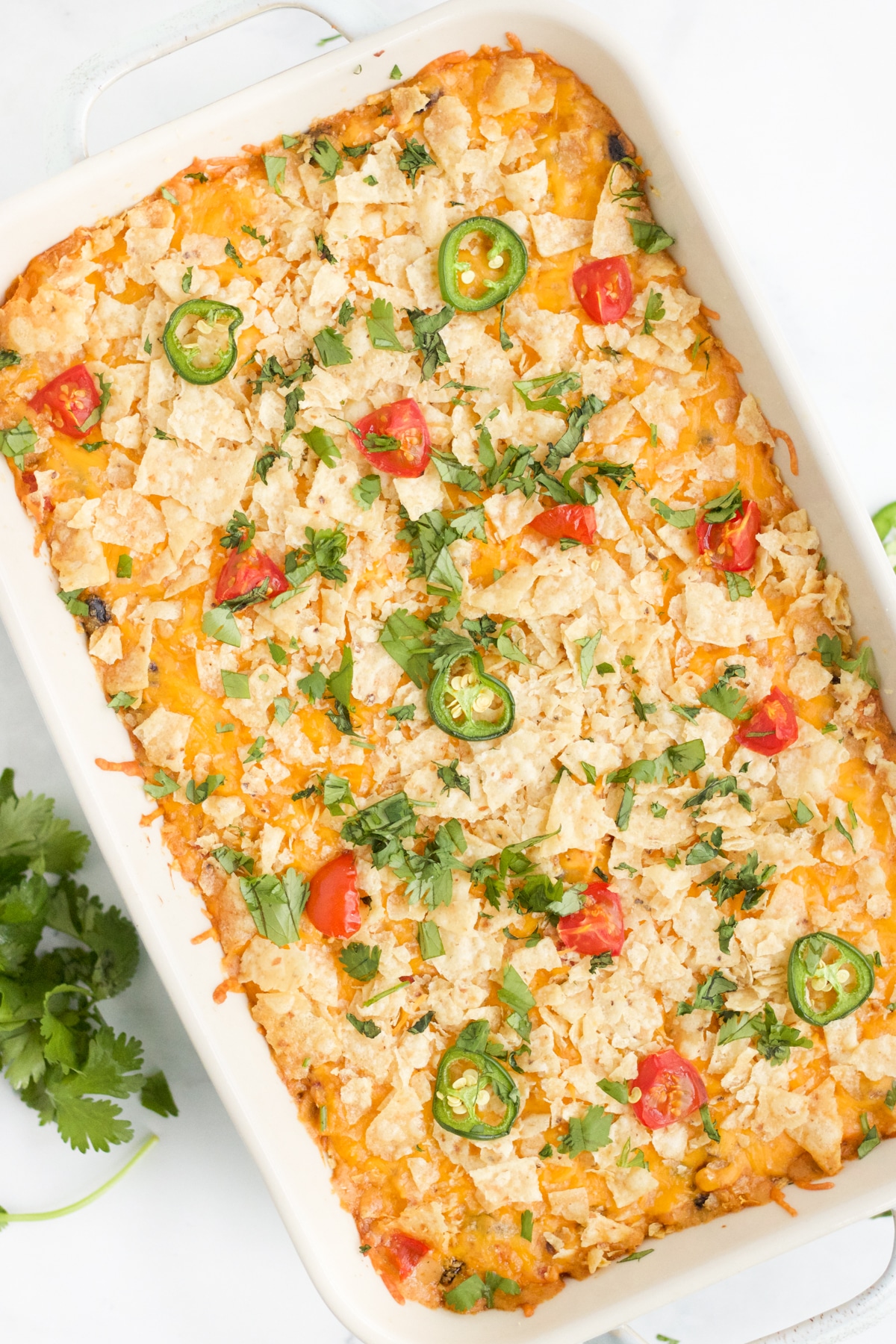 Overhead image of chicken taco casserole bake. The casserole is garnished with herbs, tomatoes and jalapeños. 