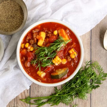 White bowl with veggie loaded chili, silver spoon, crocks of salt and pepper