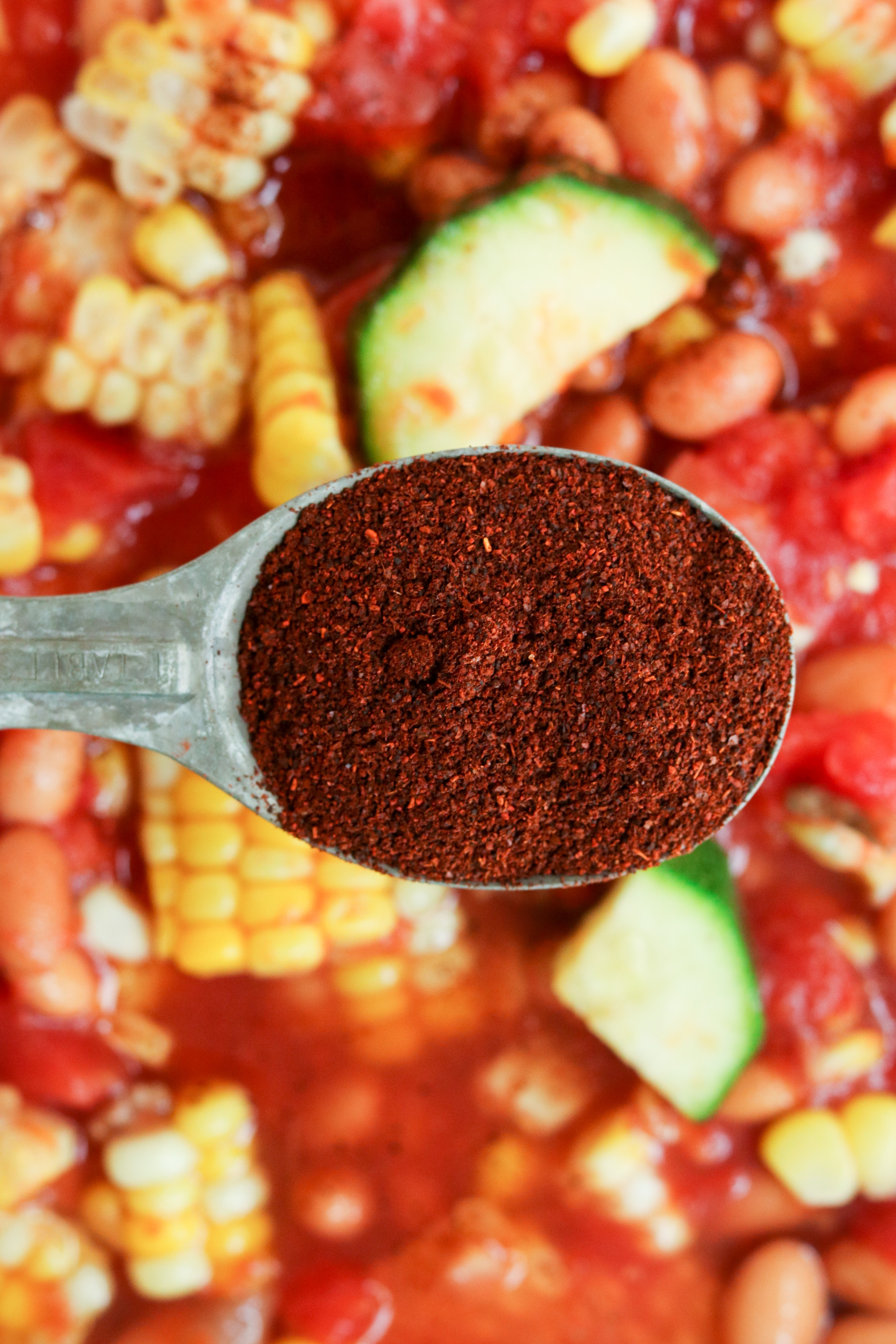 a tablespoon of chili powder being added to summer chili