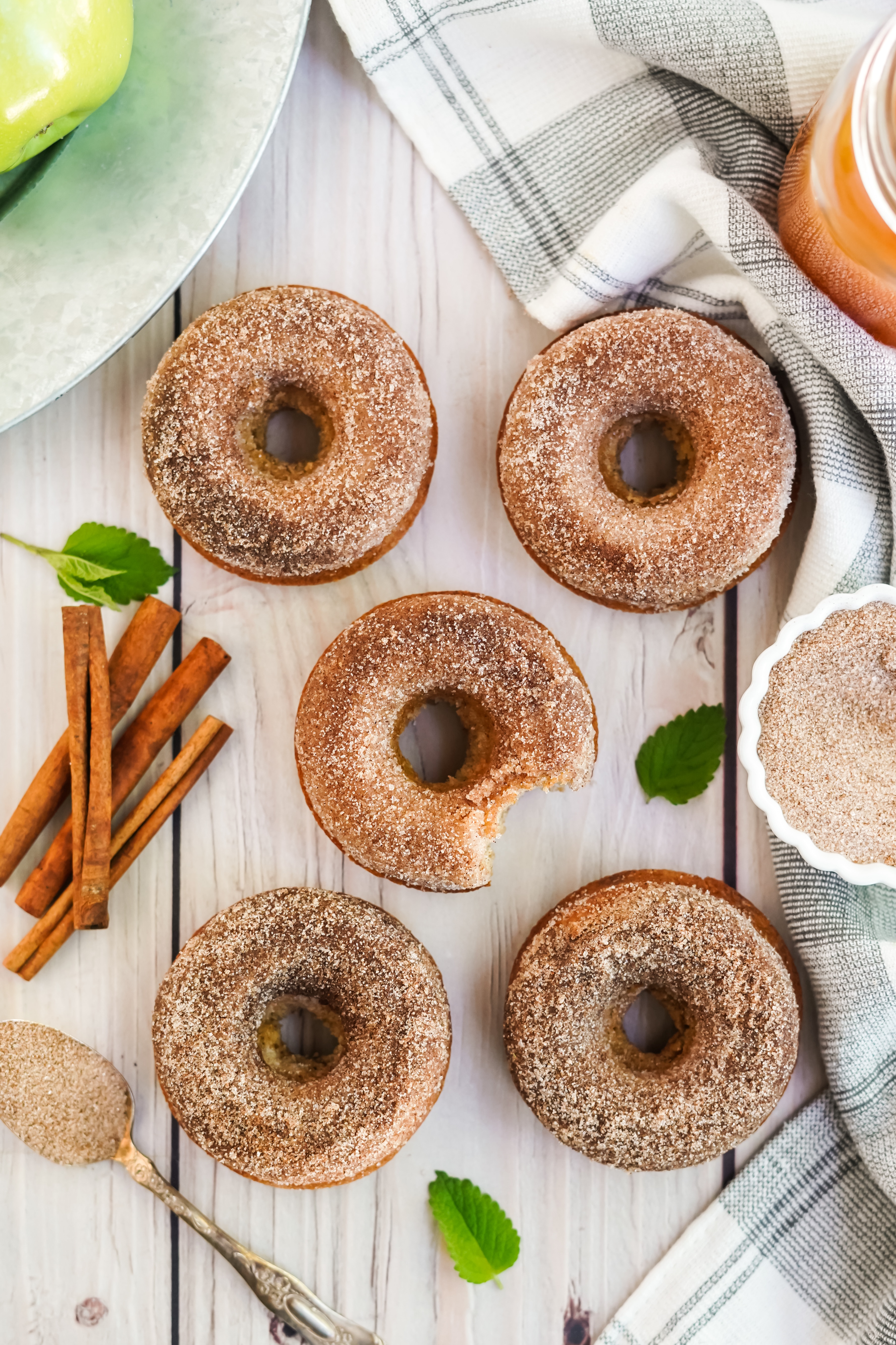 5 doughnuts with bowl of cinnamon and sugar mixtures and cinnamon sticks