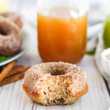 up close shot of donut with bite and glass of apple cider in background