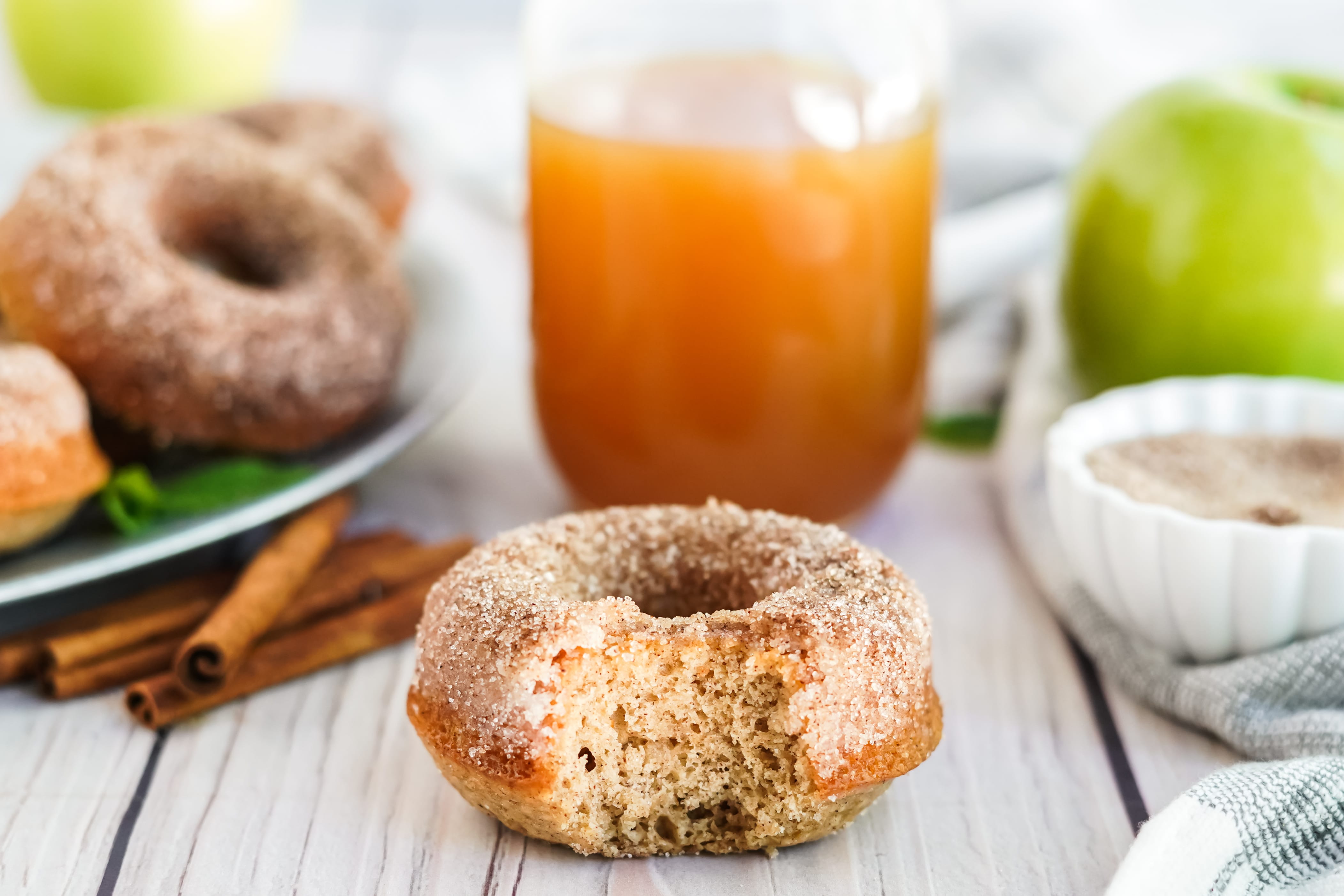 up close shot of donut with bite and glass of apple cider in background