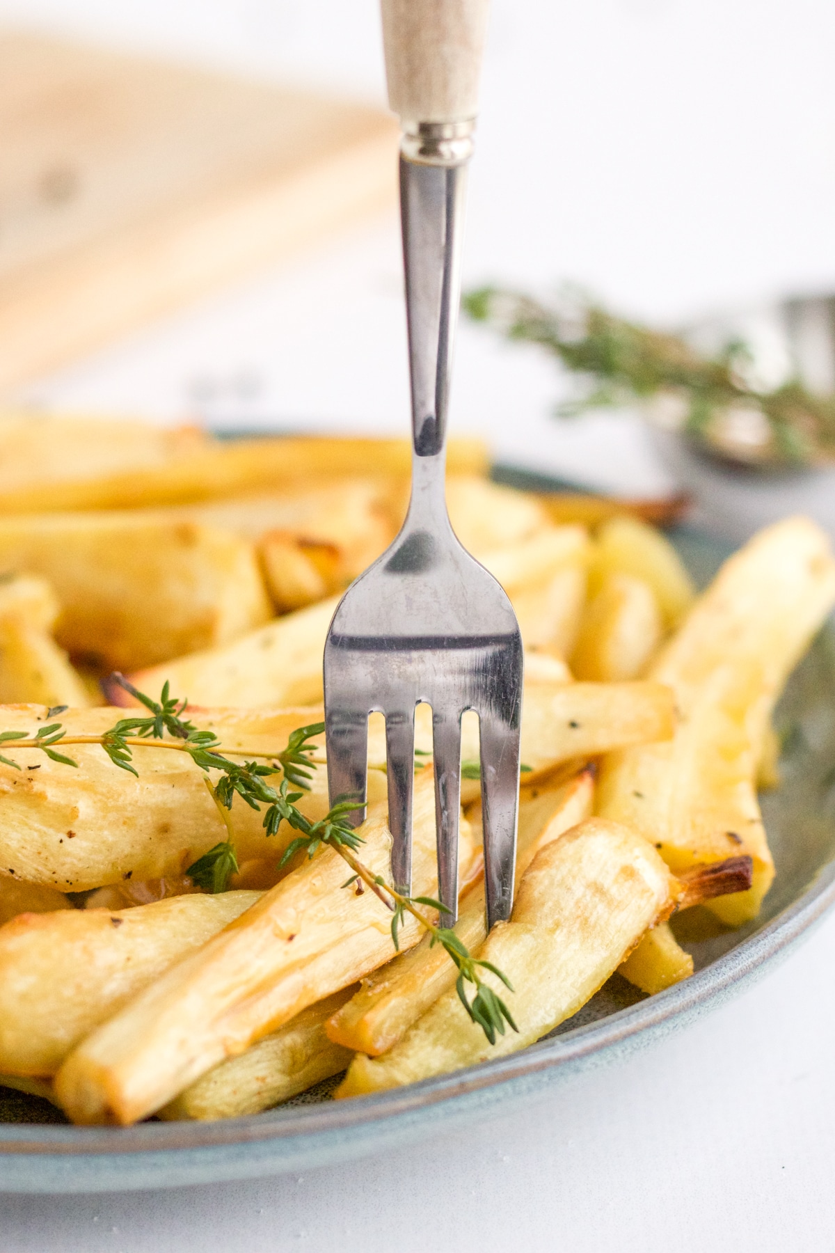 fork in a plate of roasted parsnips with thyme