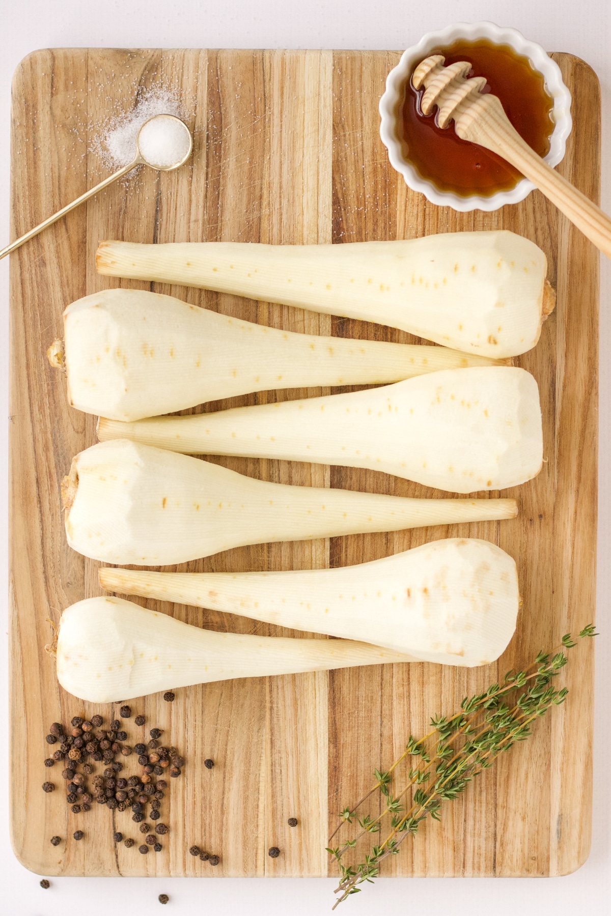 whole parsnips on wooden cutting board with honey, pepper, salt, and thyme