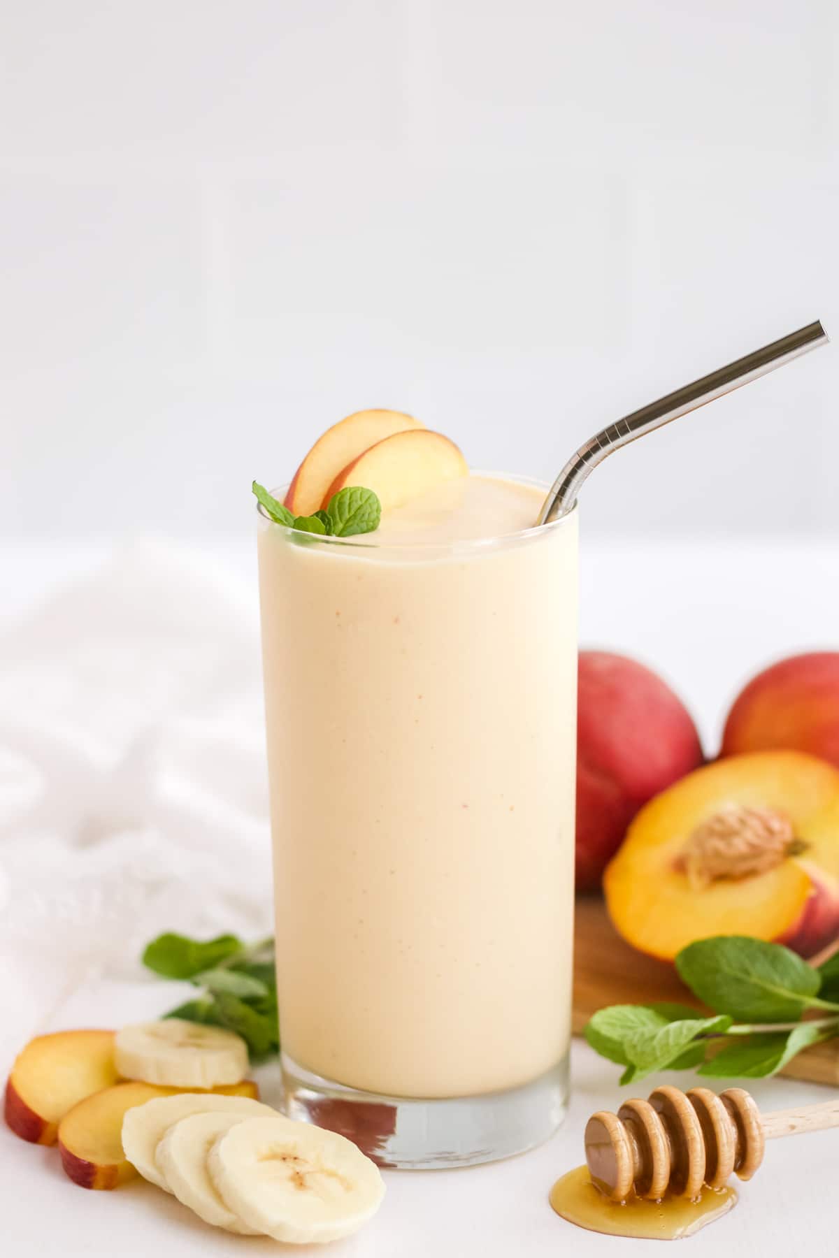 A single glass of peach smoothie garnished with peach slices and a sprig of mint. 