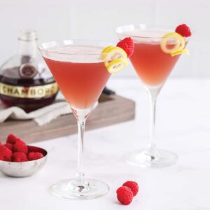 Two french twist martinis on the table with ingredients behind it.