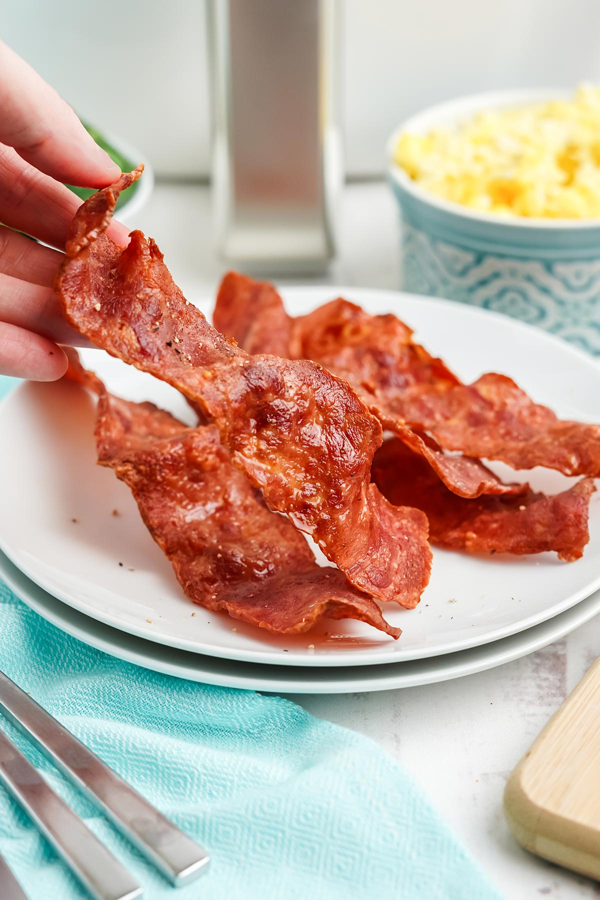 Finger picking up a piece of air fryer turkey bacon from the plate.