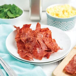 Air fryer turkey bacon on a plate with eggs and spinach in dishes behind it.