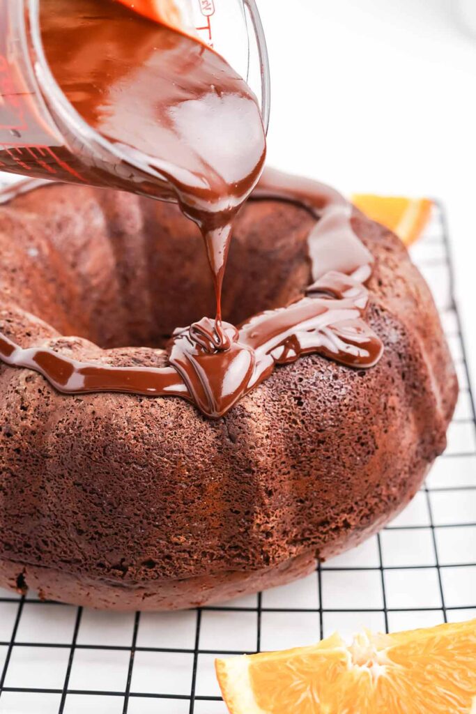 Pouring the ganache over the top of the chocolate and orange cake.