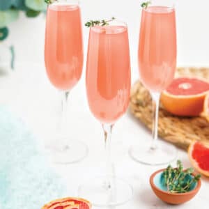 Three glasses of pink grapefruit mimosa on the table with fresh herbs on the glass as garnish.