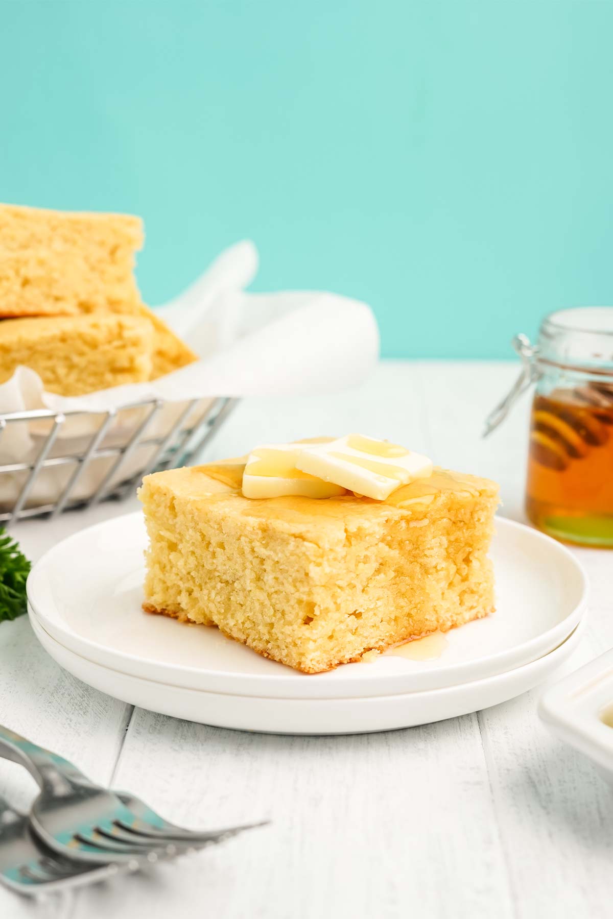 Square of cornbread with honey on a plate topped with pats of butter.