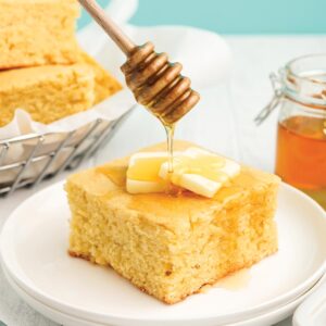 Drizzling honey over the top of a piece of cornbread with honey.