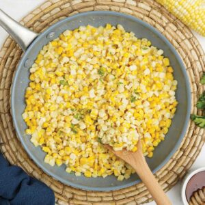 Skillet of honey butter corn with wooden spoon.