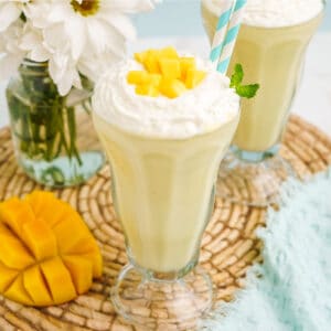 Mango shake served up in a glass with a straw and topped with whipped cream and diced mango.