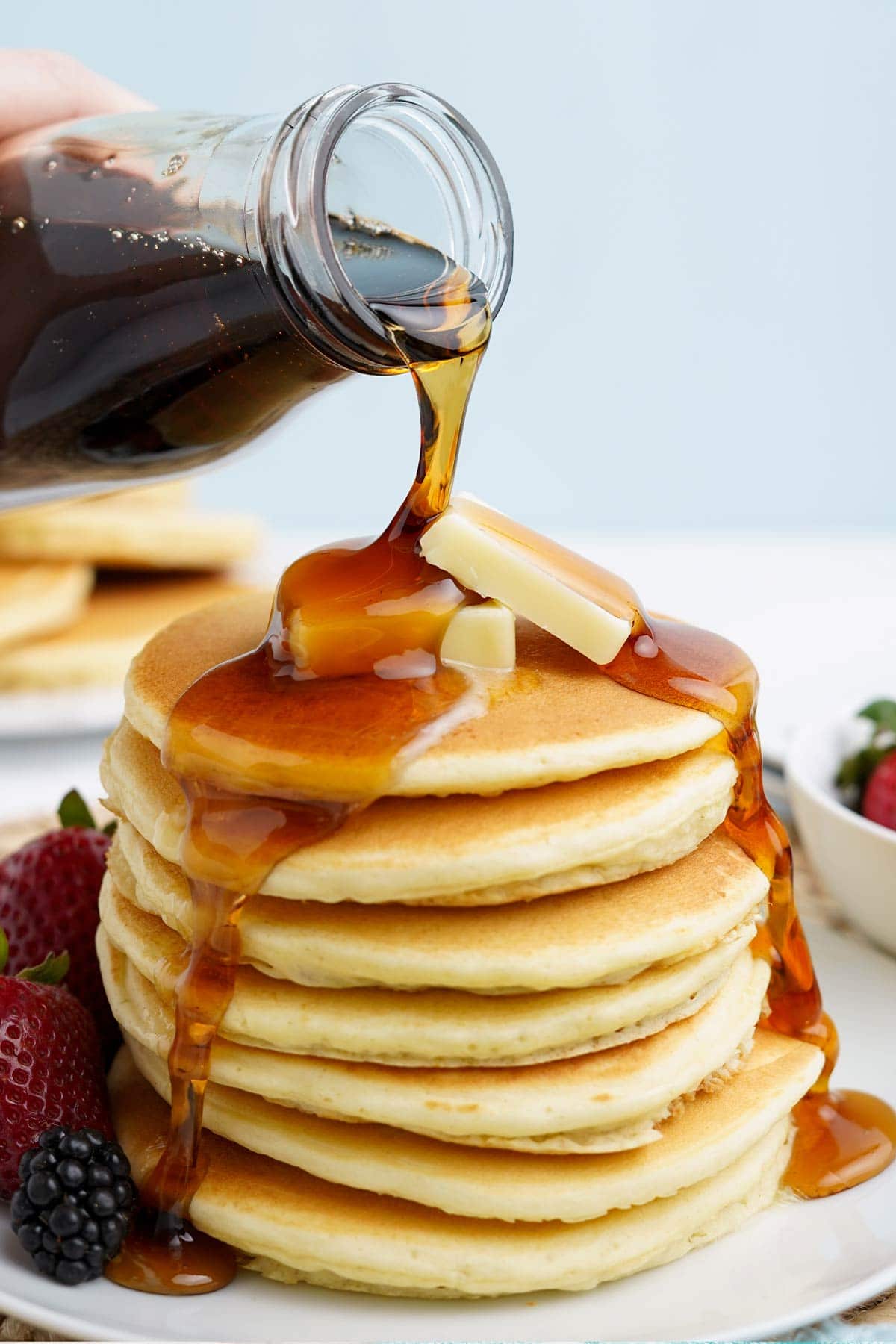 Pouring syrup over a stack of oat milk pancakes.