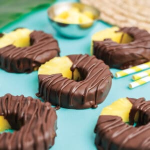 Chocolate covered pineapple on a tabletop with yellow and white straws.