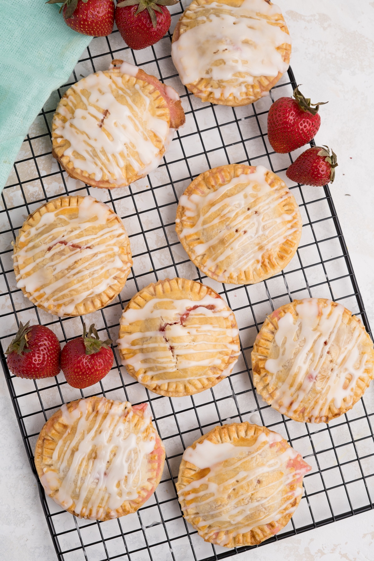 Air fryer strawberry hand pies on a cooling rack with icing and whole strawberries.