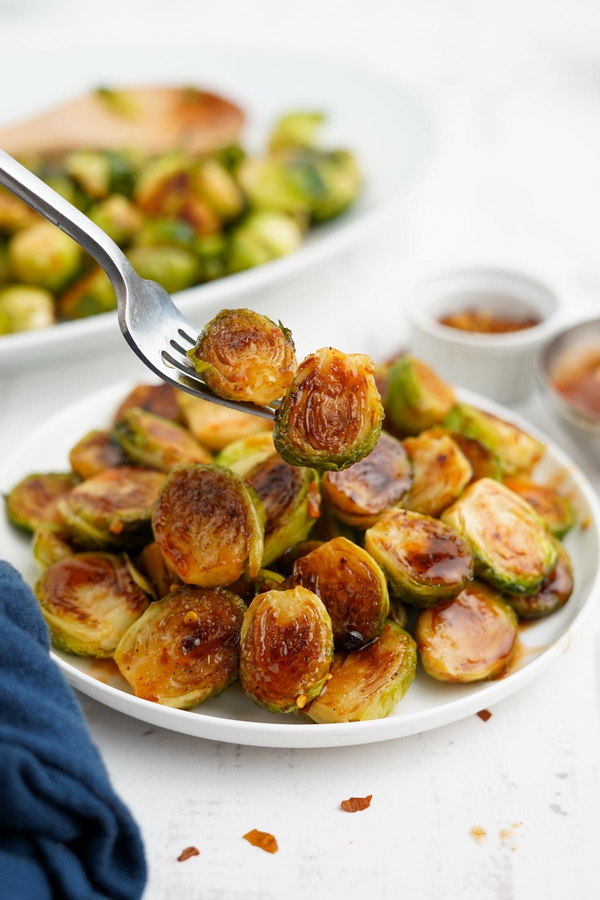 A fork holding up a bite of honey sriracha brussels sprouts over the plate.