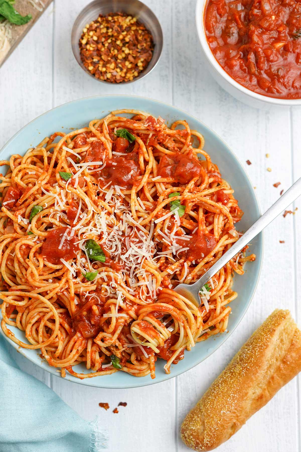Blue bowl of spaghetti arrabiata on the table with a bowl of sauce and bread.