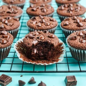 Triple chocolate muffins on a cooling rack with one in front with a bite missing.