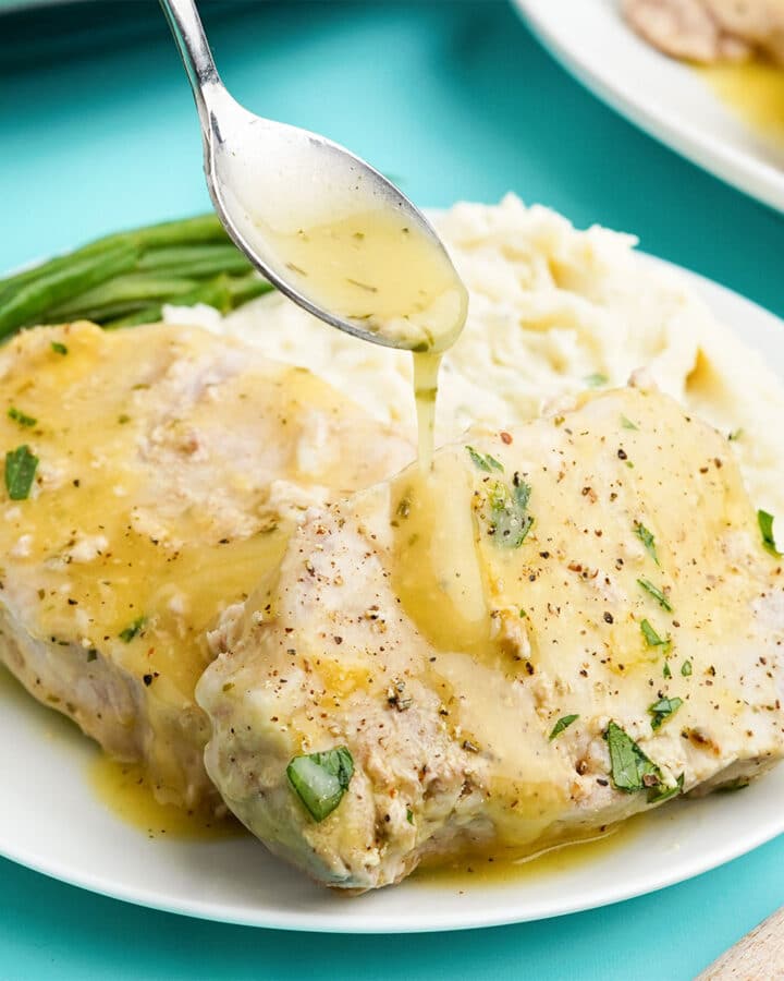 A spoon drizzling ranch gravy over a cooked pork chop.