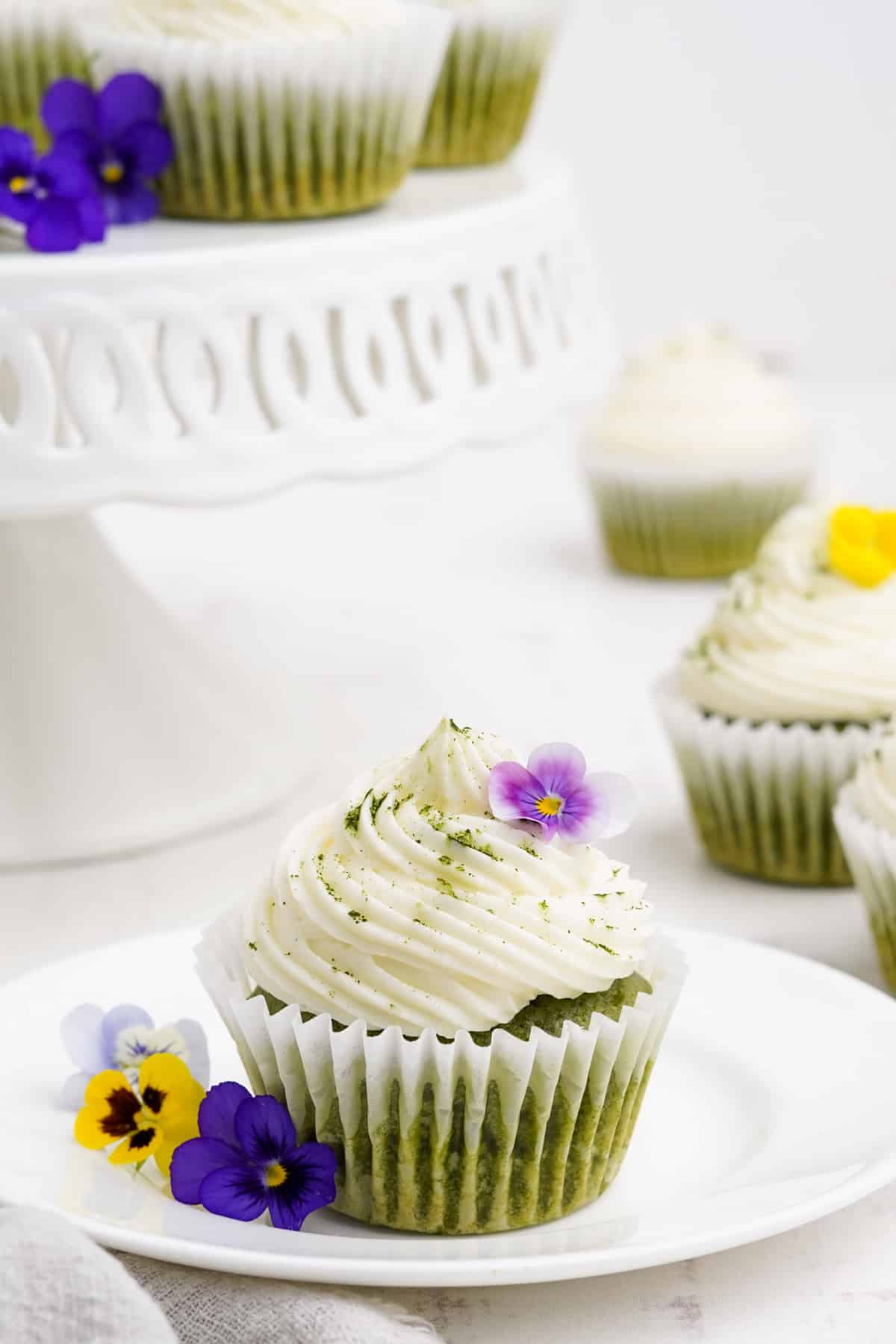 Green cupcake with white frosting on a white plate.
