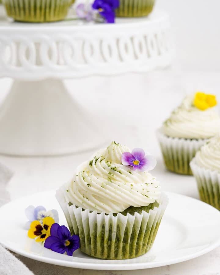 Matcha cupcake on a plate with flowers and more cupcakes in the background.