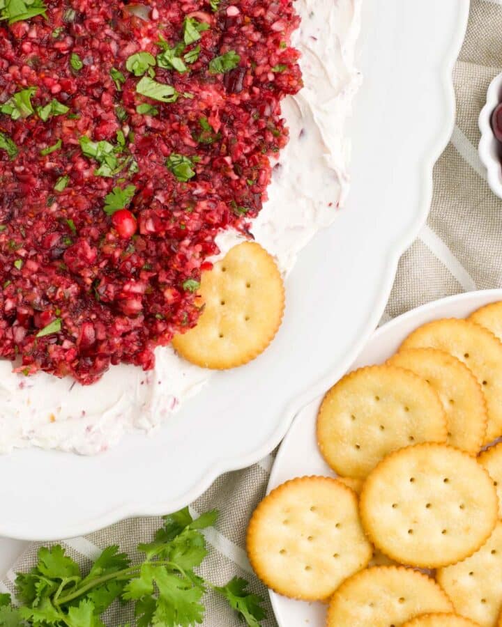 A white platter of cranberry jalapeno dip with crackers.