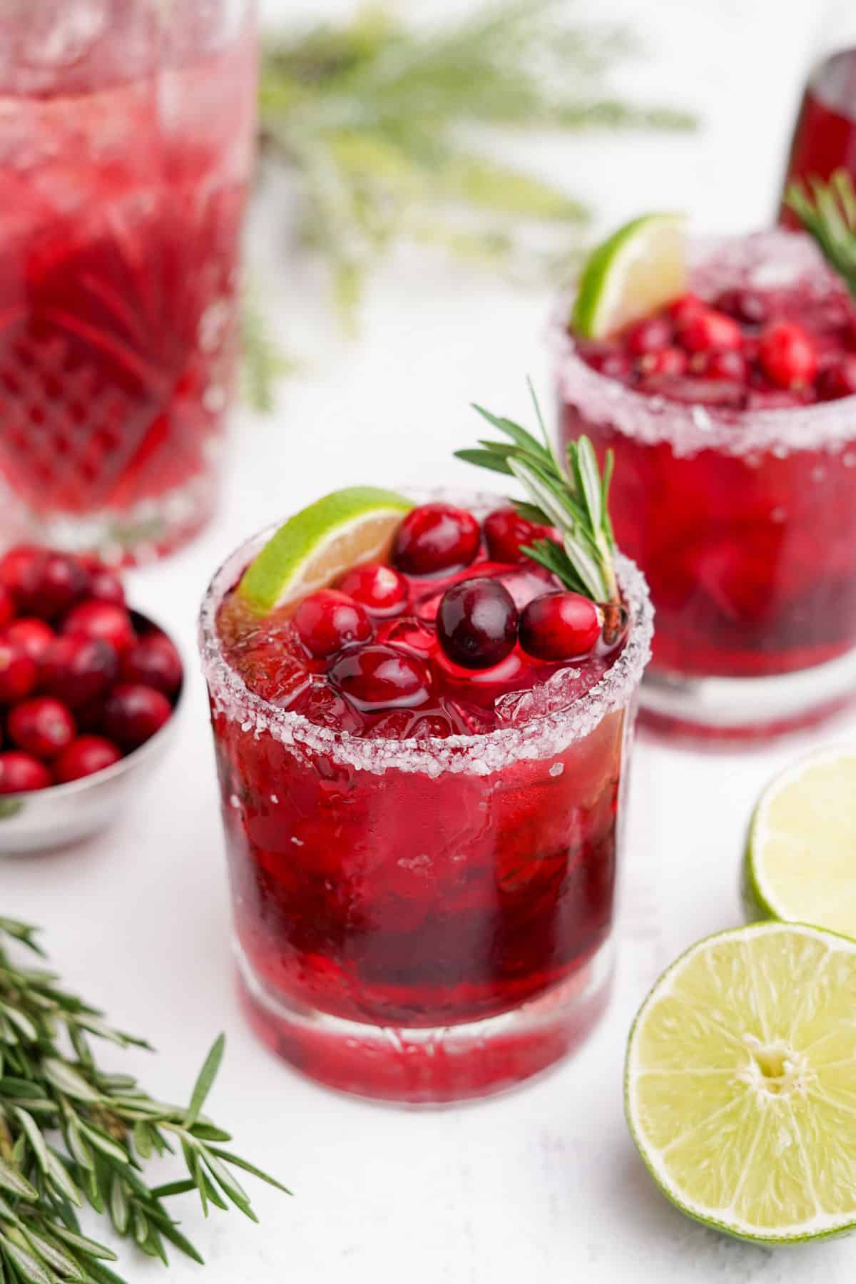 Cranberry margaritas on the table with fresh cranberries, lime wedge and rosemary.