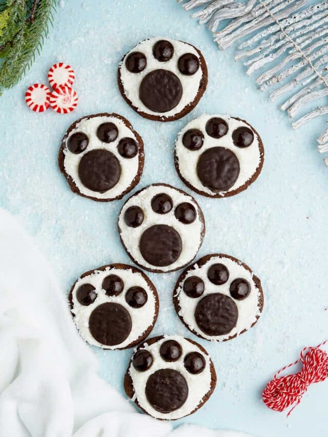 Polar bear paw print cookies on a blue surface with peppermints and snow.
