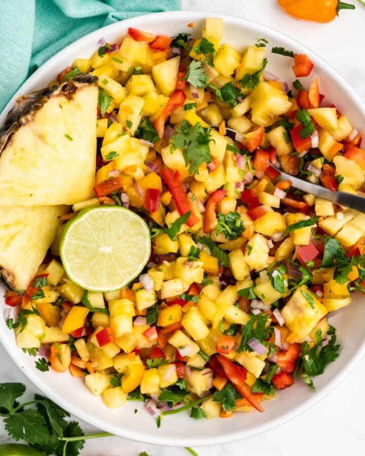 Pineapple pico de gallo in a bowl with a spoon, pineapple wedges and half a lime.