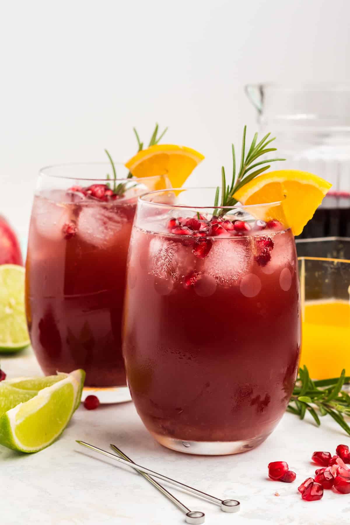 Two glasses of pomegranate mocktails on a table with orange and rosemary garnishes.
