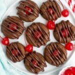 Chocolate cookies with cherries on a white plate.